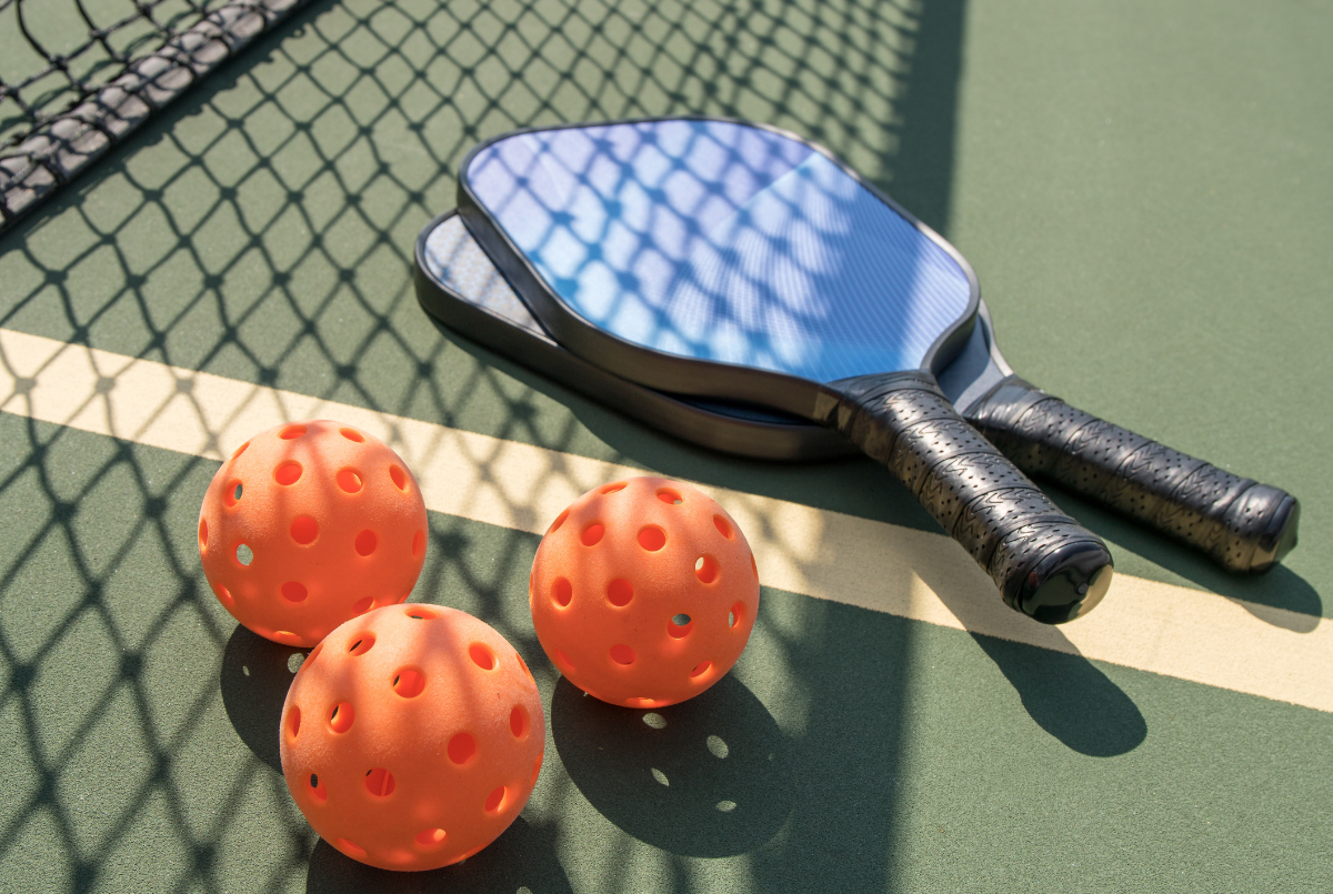 Two Blue Pickleball Paddes with three orange balls laying on the pickleball court